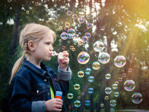 Little Girl In Park Blow Bubbles. A Lot Of Sun