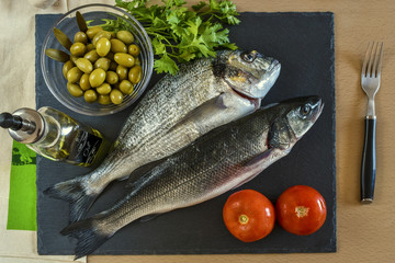 Two ready to cook raw fish with vegetables on stone slate board.