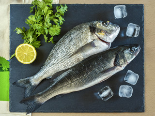Two ready to cook raw fish with lemon on stone slate board.