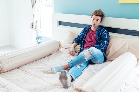 asian Man laying on the bed looking at camera.
Handsome man guy in red T-shirt and blue jeans Relaxing On Bed.