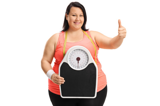 Overweight woman holding weight scale and making thumb up sign