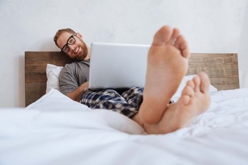 Smiling man lying in bed with laptop