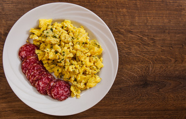 scrambled eggs with salami in a plate on wooden table with copy space. top view
