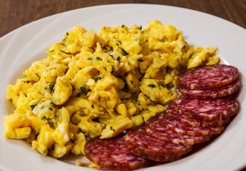scrambled eggs with salami in a plate on wooden table 