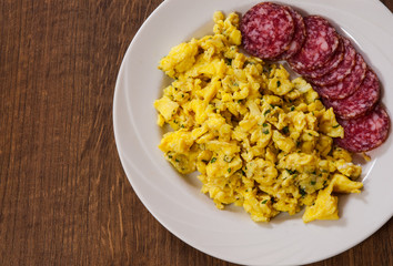 scrambled eggs with salami in a plate on wooden table with copy space. top view