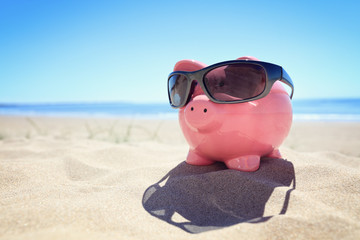 Summer piggy bank with sunglasses on the beach