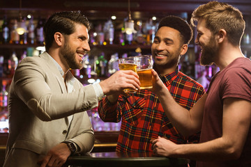 Happy smiling male friends clinking with beer mugs