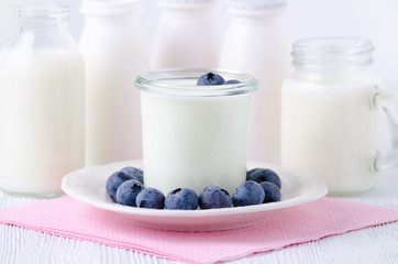 a cup of yogurt with blueberrys and different bottles of yogurt drink and milk on the table