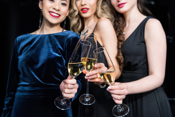 partial view of smiling women in stylish dresses clinking glasses with champagne