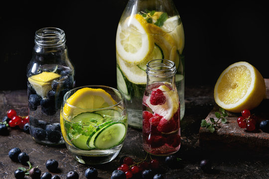 Citrus cucumber berries blueberry and raspberry sassy sassi water for detox in glass bottles on dark black background. Clean eating, healthy lifestyle concept, sunlight