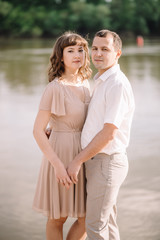 Obraz premium beautiful young couple near a large river, cuddling, standing watching with a smile, pressed against each other, in nature. summer, walk