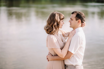 Obraz premium the girl put her arms around the man's neck, looks him in the eye on the nature near the river, a story of love, tenderness, summer, beautiful couple