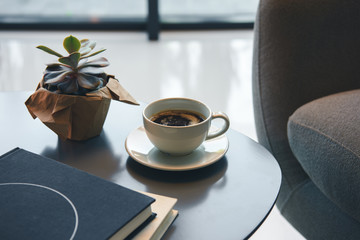 Close-up view of green succulent, cup of coffee and books on table indoors