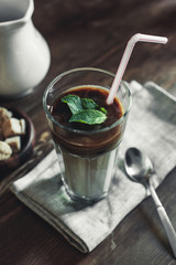 close up of latte with mint leaves, chocolate topping and straw with spoon on tabletop