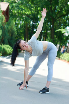 Beautiful brunette girl exercising in a green park. Training in nature. A healthy lifestyle. Sportswear.
