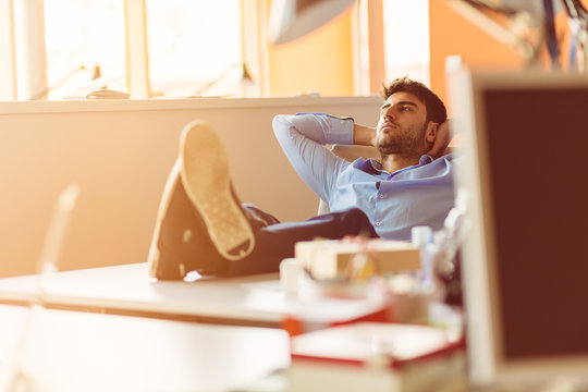 caucasian business person sitting in office thinking daydreaming hands behind head.