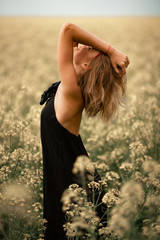 Happy young woman in black dress among flowering meadow.
