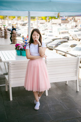 Fototapeta na wymiar Cute asian young woman in summer cafe outdoors. girl In white T-shirt, with long hair in simple light cozy interior of restaurant Urban style