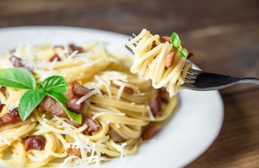 plate of Pasta Carbonara and Spaghetti with bacon and parmesan cheese on a fork on old wooden table