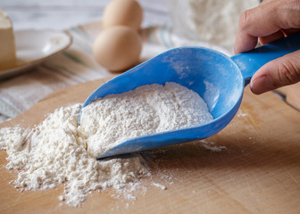 Wheat flour in blue plastic spoon on wooden board
