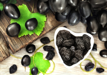Dried black raisins in heart-shaped bowl with fresh organic grapes