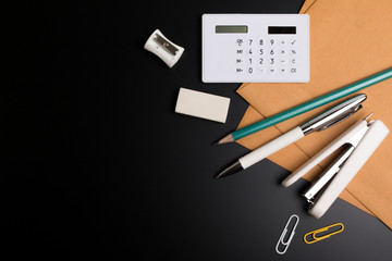 Office desk table with office supplies pencil, eraser, pencil sharpener, envelope and calculator on black office paper. Black and white office desk style. Top view with copy space for text.