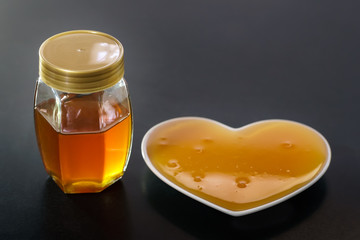 Honey is poured into a heart shape plate with glass jar
