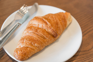 Warm fresh Croissants on a white plate with fork and knife in the coffee shop.(Selective focus with shallow depth of field)