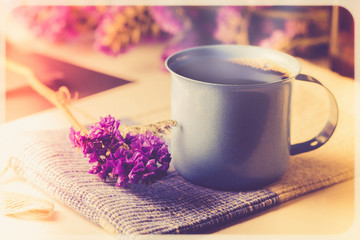 Fototapeta na wymiar Violet dried flowers and blue cup coffee on wooden table with vintage image style and soft light