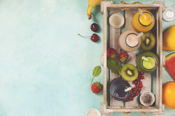Fresh juices or smoothies with fruits and vegetables in wooden tray on blue background