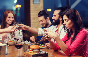 woman with smartphone and friends at restaurant