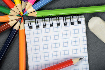 colored pencils, eraser, notebook closeup on wooden table