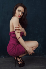Beautiful girl in red dress sits on dark background. Fallfashion. VogueStyle.