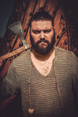 Viking with axe standing near drakkar on the seashore.