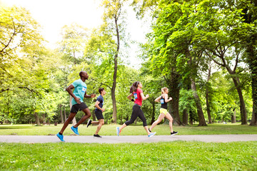 Group of young athletes running in green sunny park.