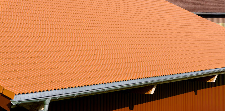 Red tiles roof with rain pipe and corrugated metal wall.