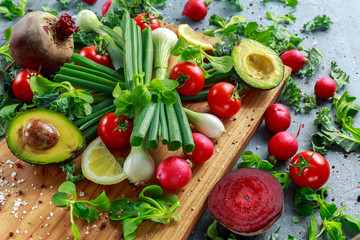 Seasonal vegetables ingredient for salad, red radish, tomatoes, spring onions, beetroot, lemons and avocado on oak cutting board with sea salt and corn peppers