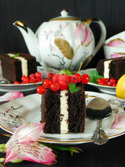 Three cakes on the plates surrounded by flowers, lemons, berries and the tea set