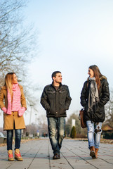 Two young teenage girls and one guy walking down the street and talk