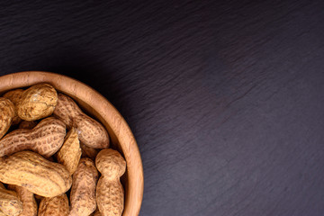 Peanuts lie in a wooden cup on a black stone board in the form of a frame, space for text