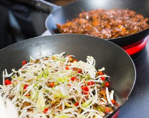 Row of woks with cooked food on portable heating devices