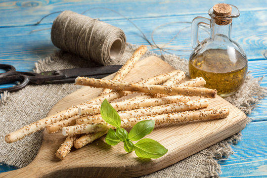 Fresh baked grissini bread sticks on wooden cutting board.