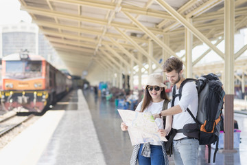 Fototapeta premium Young couple asian woman and caucasian man traveler are looking the map with train station background. Travel in summer concept.