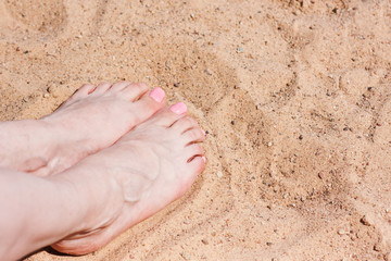 Legs of a girl on a sandy beach by the sea sunbathing. Sand and sea water. Relax by the sea on the beach. Vacation. Relaxation, bathing. Hot weather. The background
