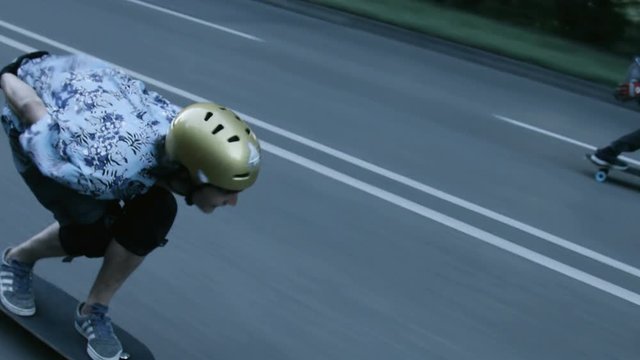 A dolly shot of two skateboarders as they speed down a street in Stuttgart. Cars drive by on the opposing street lane as the skateboarder gain momentum through speed tucks.