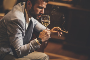 Young man tasting white wine and smoking cigar