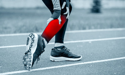 Athletic woman on running track has calf cramp and touching hurt leg