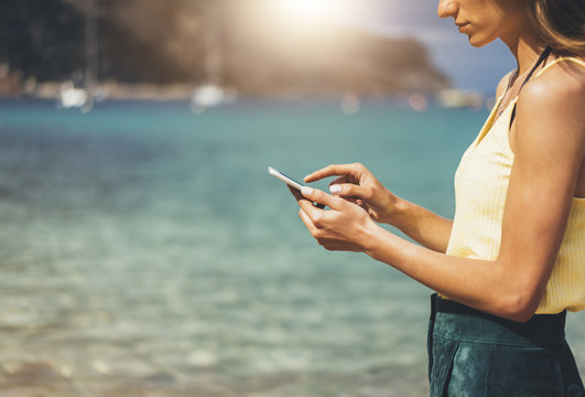 Hipster girl hold on smart phone gadget in sand coastline screen. Traveler using in female hand mobile on background beach seascape horizon. Tourist look on blue sun ocean, summer lifestyle