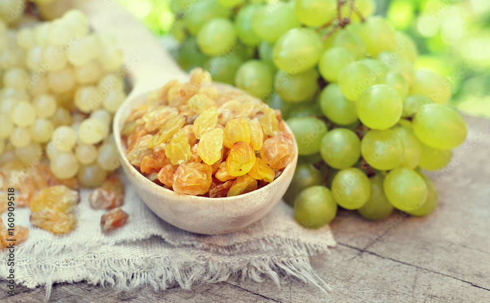 Wall mural Dried yellow raisins in wooden spoon with fresh ripe grapes