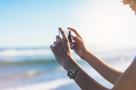 Hipster girl photograph on smart phone gadget in sand coastline, mock up of blank screen. Traveler hold and using in female hand mobile on background seascape horizon on blue sun ocean, lifestyle